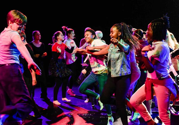 Mehrere Jugendliche tanzen fröhlich auf der Bühne.